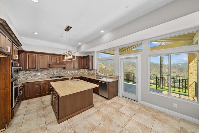 kitchen with dishwasher, pendant lighting, sink, a kitchen island with sink, and light stone countertops