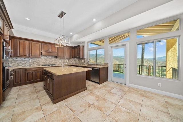 kitchen with decorative light fixtures, a mountain view, a kitchen island with sink, stainless steel appliances, and light stone counters