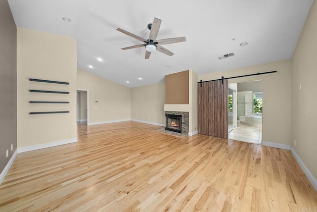 unfurnished living room featuring lofted ceiling, a stone fireplace, ceiling fan, light hardwood / wood-style flooring, and a barn door