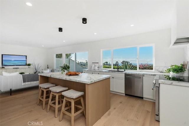 kitchen featuring white cabinets, dishwasher, a kitchen island, sink, and light stone counters