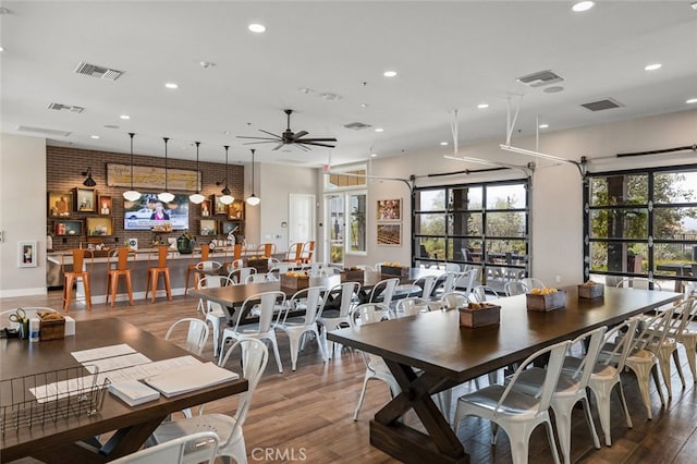 dining space with ceiling fan, brick wall, and wood-type flooring