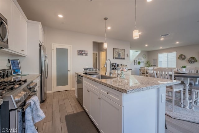 kitchen featuring sink, pendant lighting, white cabinets, and a kitchen island with sink