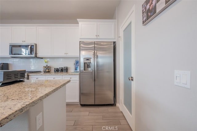 kitchen with tasteful backsplash, white cabinets, light stone counters, and stainless steel appliances