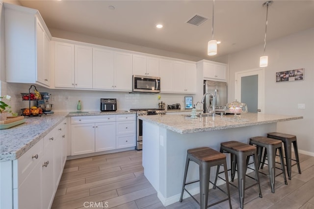 kitchen with white cabinetry, stainless steel appliances, pendant lighting, and a center island with sink