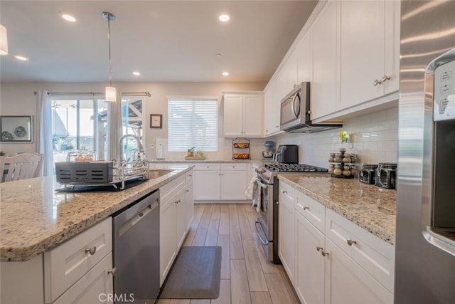 kitchen featuring stainless steel appliances, pendant lighting, white cabinets, and light stone counters