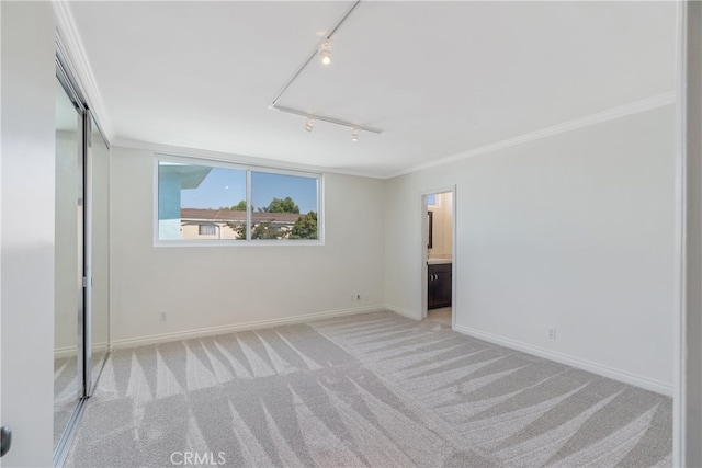 unfurnished bedroom featuring ensuite bath, light carpet, rail lighting, a closet, and ornamental molding