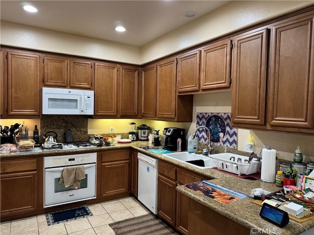 kitchen with decorative backsplash, white appliances, light tile patterned flooring, stone counters, and sink