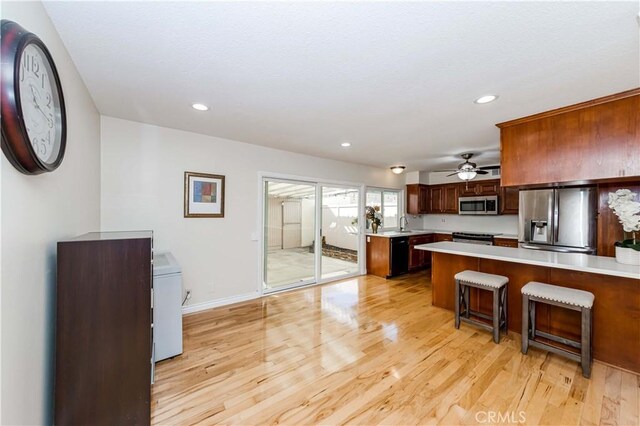 kitchen with appliances with stainless steel finishes, light countertops, light wood-style floors, and a peninsula