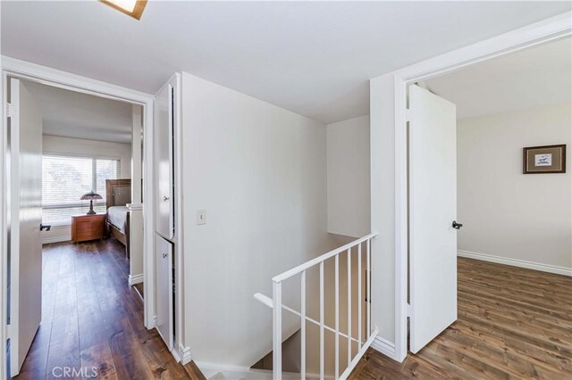 corridor with dark wood-style flooring, an upstairs landing, and baseboards