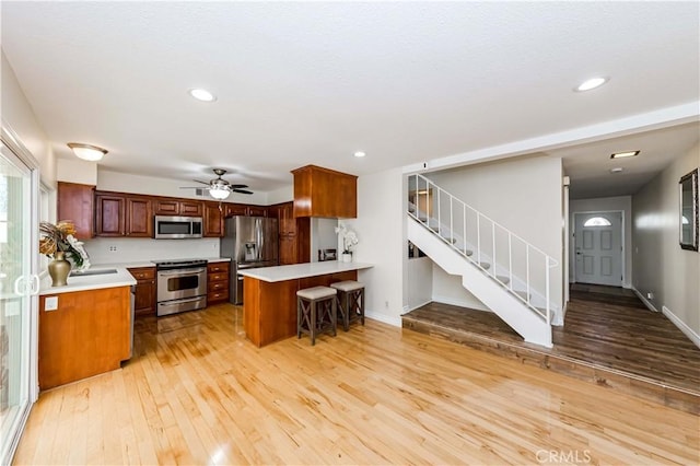 kitchen featuring stainless steel appliances, a peninsula, light countertops, light wood-type flooring, and a kitchen bar