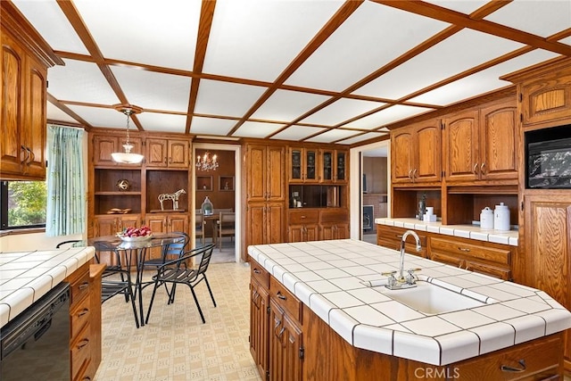 kitchen with pendant lighting, black appliances, sink, tile countertops, and a center island with sink