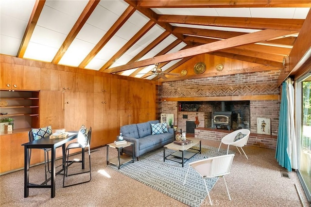 living room featuring light carpet, a wood stove, wood walls, ceiling fan, and beam ceiling