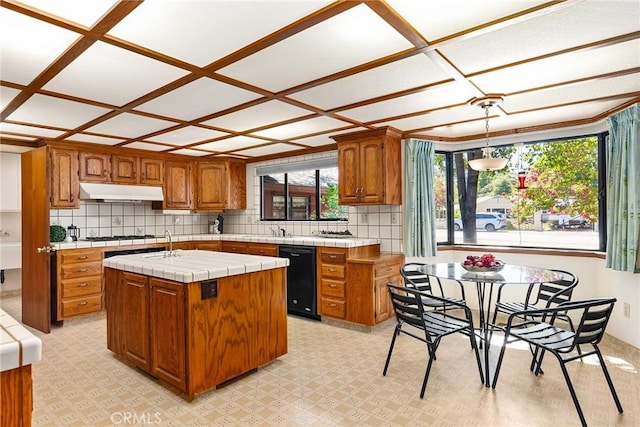 kitchen with tile countertops, black dishwasher, tasteful backsplash, and a kitchen island with sink