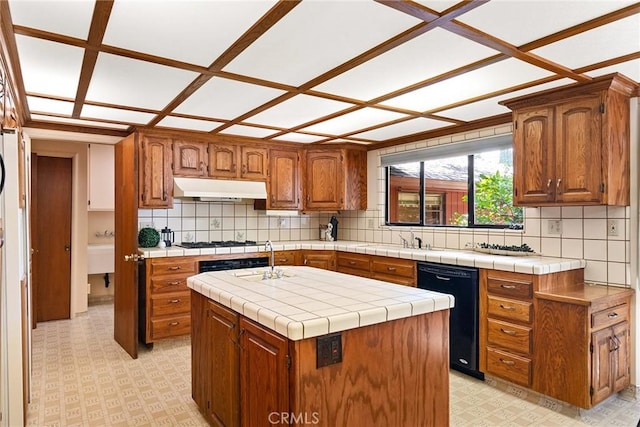 kitchen featuring tile counters, black dishwasher, sink, backsplash, and a center island with sink