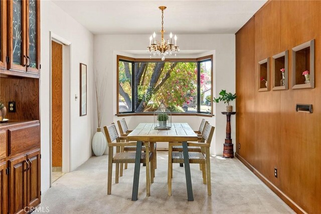 dining room featuring light colored carpet, a chandelier, and wooden walls