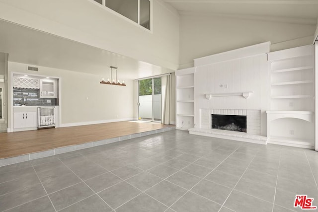 unfurnished living room featuring a brick fireplace, a high ceiling, beverage cooler, and tile patterned flooring