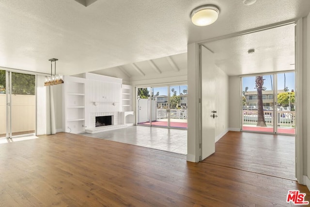 unfurnished living room featuring a textured ceiling, lofted ceiling, dark wood-type flooring, built in shelves, and a brick fireplace