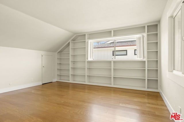 additional living space with lofted ceiling, built in features, and hardwood / wood-style flooring