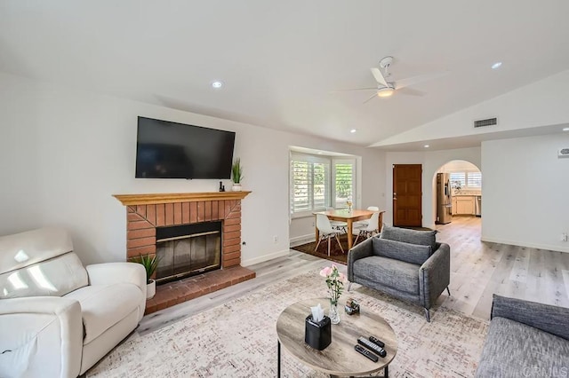 living room featuring lofted ceiling, light wood-type flooring, a brick fireplace, and ceiling fan