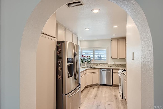 kitchen with cream cabinets, sink, stainless steel appliances, and light hardwood / wood-style flooring