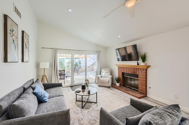 living room with lofted ceiling, light wood-type flooring, a brick fireplace, and ceiling fan