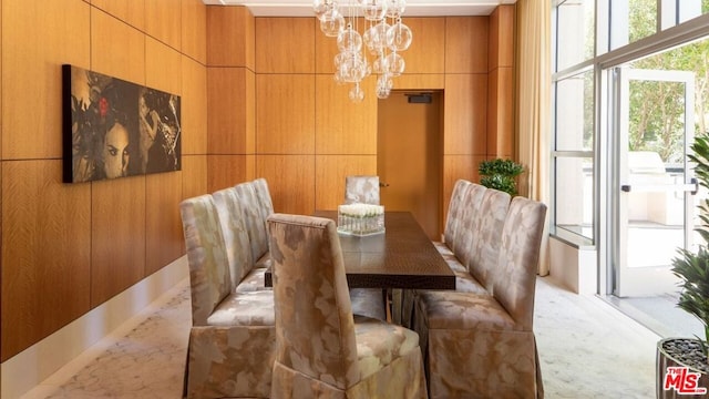 carpeted dining area featuring a notable chandelier and wood walls