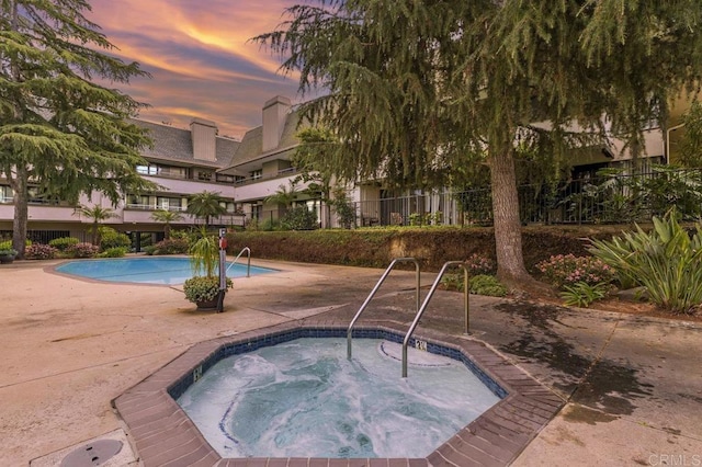 pool at dusk featuring a hot tub