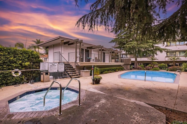 pool at dusk featuring a patio area and a community hot tub