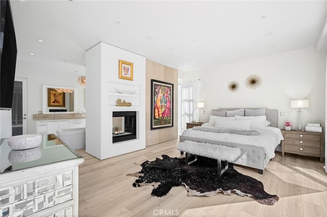 bedroom featuring ensuite bathroom, a multi sided fireplace, and light hardwood / wood-style floors