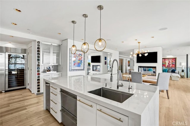 kitchen with white cabinetry, wine cooler, sink, a kitchen island with sink, and light stone counters