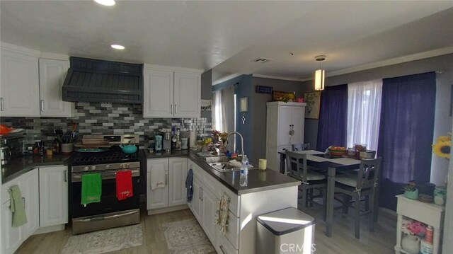 kitchen with premium range hood, white cabinetry, stainless steel range with gas cooktop, and sink