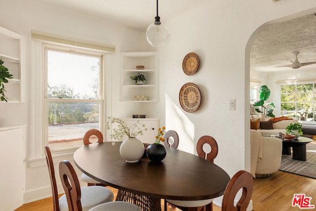 dining room featuring built in shelves, light hardwood / wood-style floors, and a textured ceiling