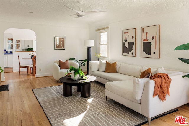 living room featuring a textured ceiling, ceiling fan, and light wood-type flooring