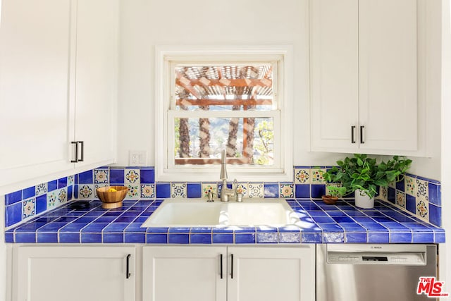 kitchen with white cabinetry, sink, backsplash, stainless steel dishwasher, and tile counters