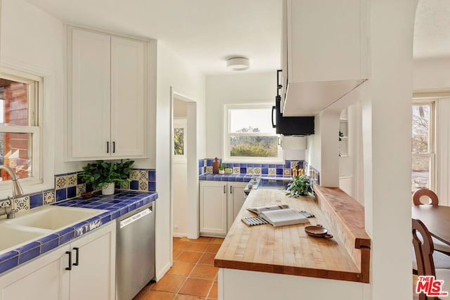 kitchen featuring light tile patterned flooring, tile countertops, white cabinetry, sink, and stainless steel dishwasher