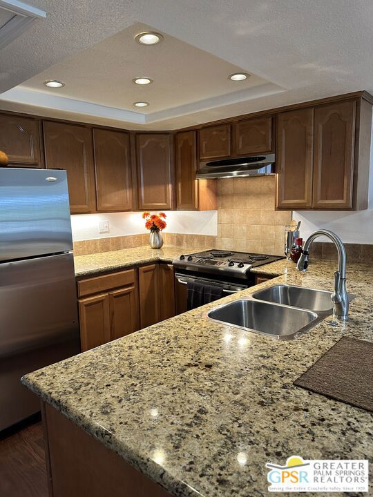 kitchen featuring stainless steel appliances, dark hardwood / wood-style flooring, light stone countertops, and sink