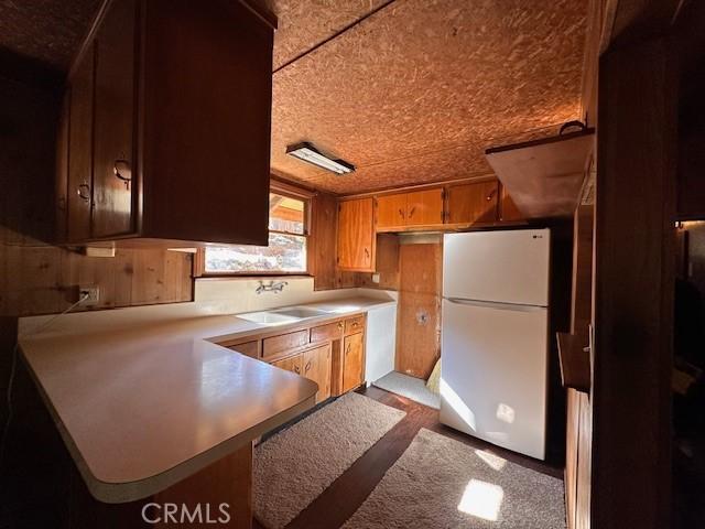 kitchen featuring a peninsula, a sink, light countertops, and freestanding refrigerator