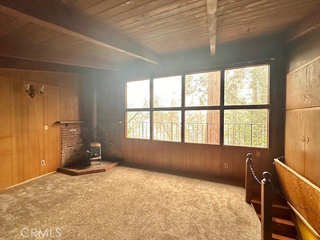 interior space with wood walls, a wood stove, wooden ceiling, beamed ceiling, and carpet flooring