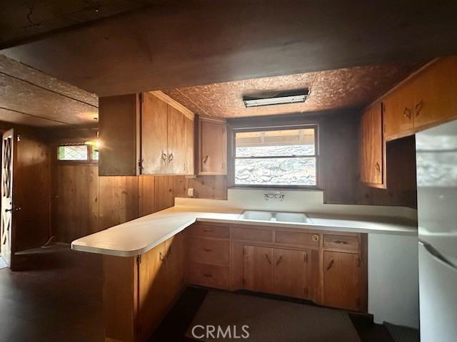 kitchen featuring wood walls, a sink, light countertops, a peninsula, and freestanding refrigerator