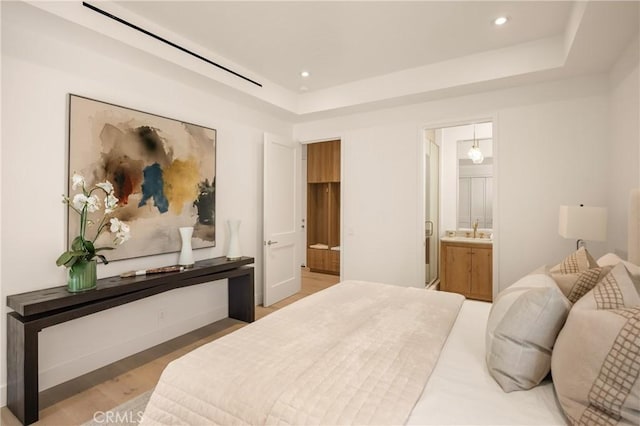 bedroom featuring a tray ceiling, connected bathroom, and hardwood / wood-style floors