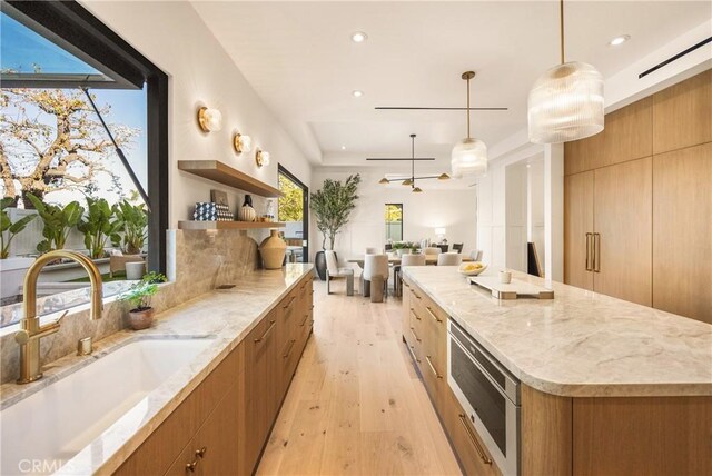 kitchen with a spacious island, sink, decorative light fixtures, light stone countertops, and light hardwood / wood-style floors