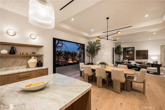 kitchen with decorative light fixtures, light stone countertops, a raised ceiling, and a kitchen island