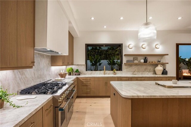 kitchen with wall chimney exhaust hood, sink, double oven range, pendant lighting, and light stone countertops