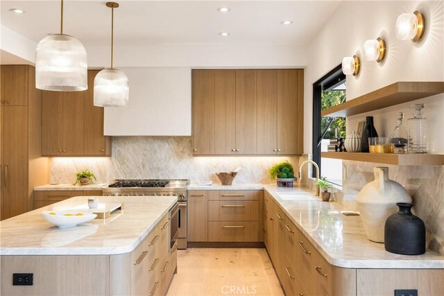 kitchen with sink, tasteful backsplash, high end stainless steel range, a kitchen island, and decorative light fixtures