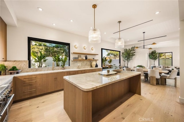 kitchen with decorative light fixtures, sink, backsplash, a center island, and light hardwood / wood-style flooring