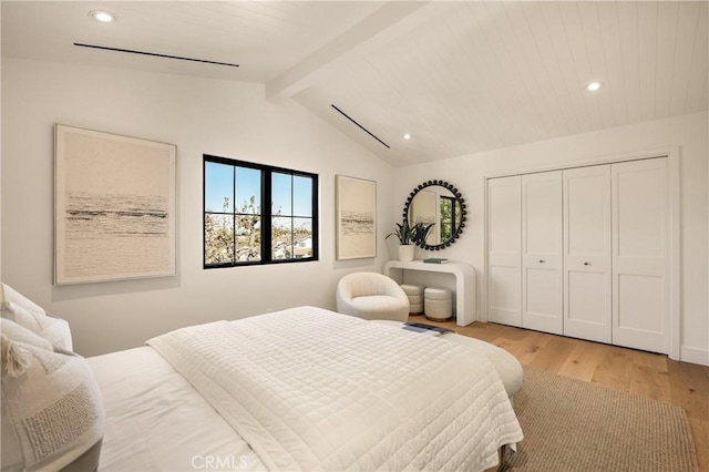 bedroom featuring lofted ceiling with beams, light hardwood / wood-style floors, and a closet