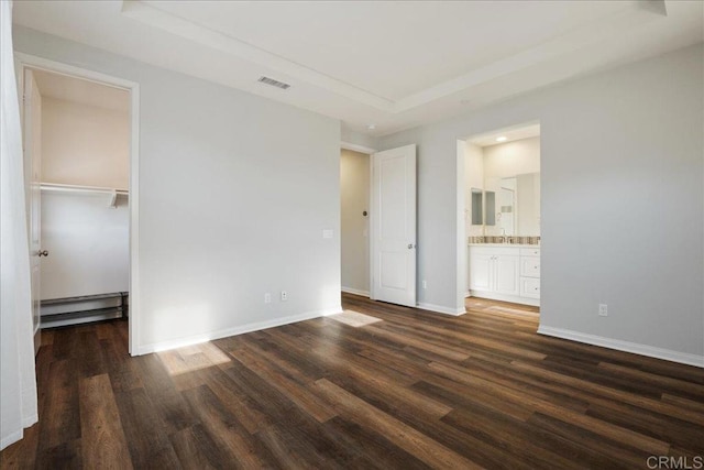 unfurnished bedroom featuring ensuite bath, a baseboard heating unit, a spacious closet, and dark hardwood / wood-style floors