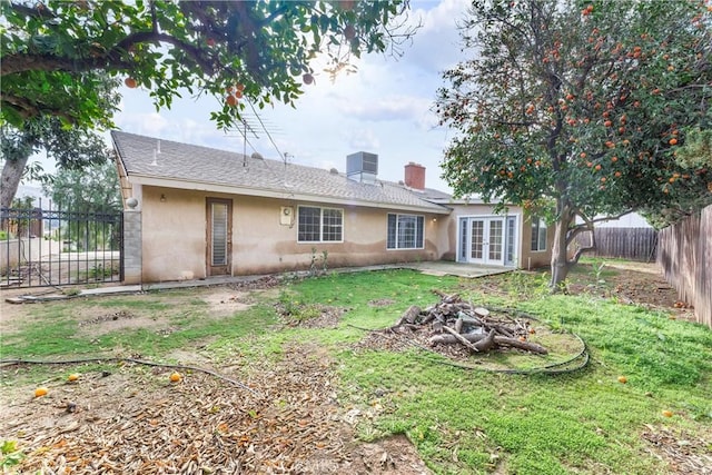 back of property with central AC unit, an outdoor fire pit, french doors, and a lawn