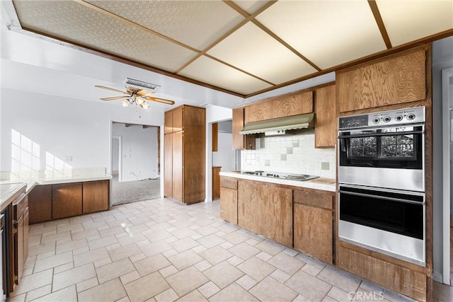 kitchen featuring ceiling fan, decorative backsplash, cooktop, stainless steel double oven, and wall chimney exhaust hood