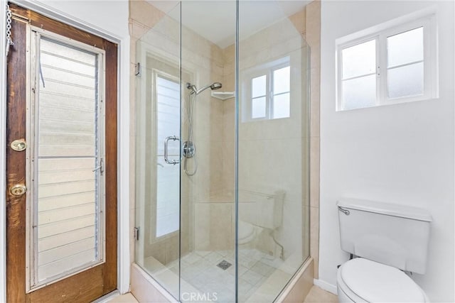 bathroom with a shower with shower door, toilet, and a healthy amount of sunlight